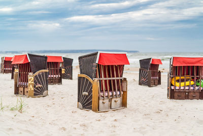 Hooded beach chairs on shore at beach against sky