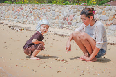 Full length of mother and son crouching on sand at beach