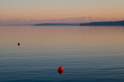 Red balloons in sea against sky during sunset