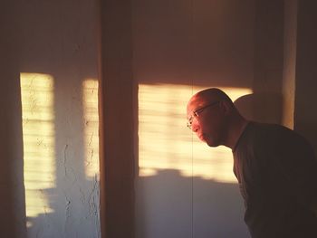 Side view of young man standing against window