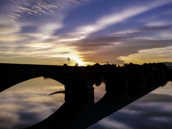 Silhouette bridge over lake against sky during sunset