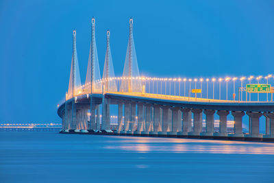 Illuminated bridge over sea against sky at dusk