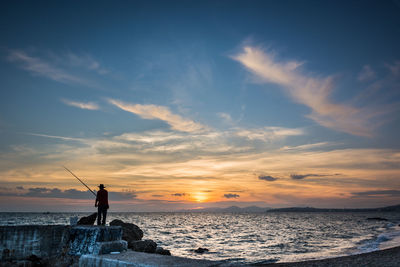 Silhouette man fishing on beach against sky during sunset