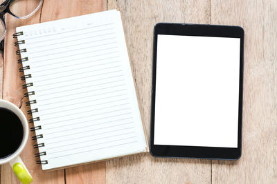 Directly above shot of digital tablet and spiral notebook on table