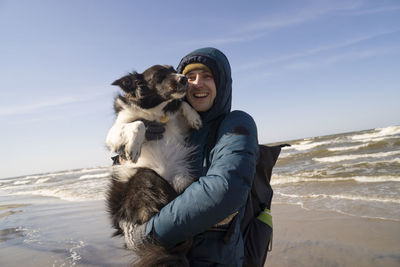 Happy young man carrying pet dog at beach on sunny day