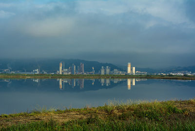 View of factory by lake against sky