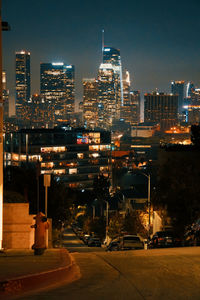 Illuminated street amidst buildings against sky at night