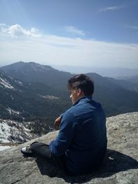 Man sitting on mountain against sky