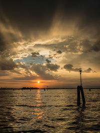 Silhouette man in sea against sky during sunset