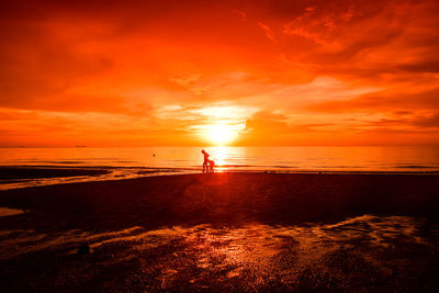 Silhouette man standing on beach against orange sky