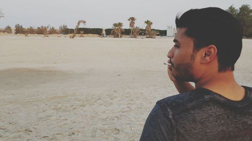 Young man smoking on beach against sky