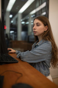 Side view of young woman using computer while sitting on table