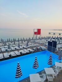 Lifeguard chair and lounge chairs at resort by sea against sky