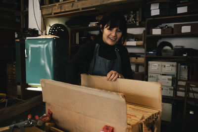Smiling female entrepreneur opening box in workshop