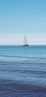 Sailboat in sea against clear blue sky