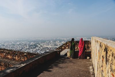 Rear view of woman standing on railing against sky