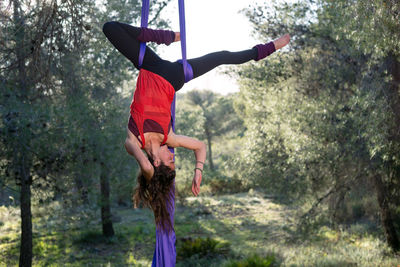 Young girl acrobat. practicing aerial silks. woman doing circus stunts with clothes in the forest. inverted hip lock position.