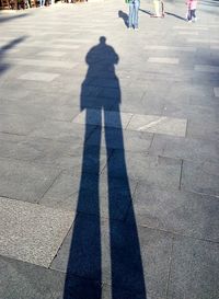 People and shadow on road during sunny day