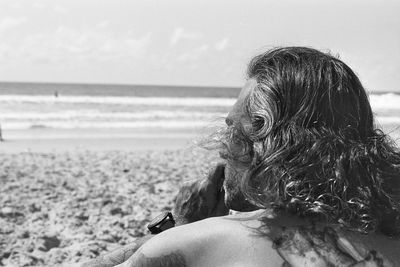 Rear view of man sitting at beach against sky