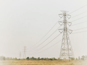 Low angle view of electricity pylon on field against clear sky