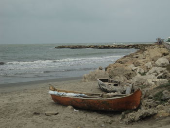 Boat moored on shore by sea against sky