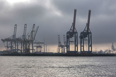 Cranes at commercial dock against sky