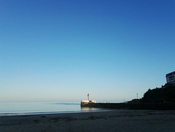 Lighthouse by sea against clear blue sky