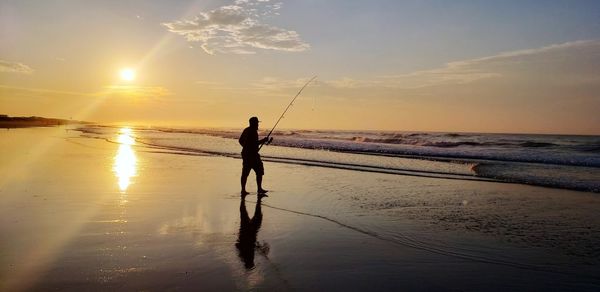 Silhouette man fishing at beach during sunset