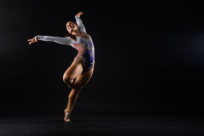 Full length of woman exercising against black background