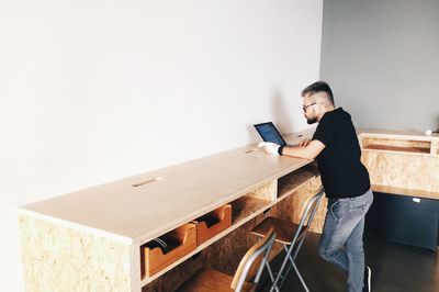 Man standing by table while using laptop