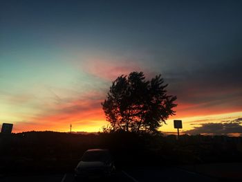 Silhouette trees by road against sky during sunset