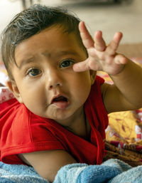 Cute indian baby lying on bed sheet over a mat extending arm towards the camera.