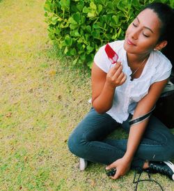 Young woman sitting on grass against plants