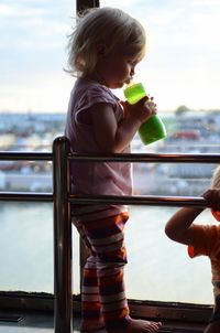 Side view of girl having drink while standing by railing