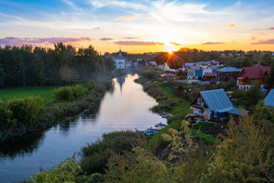 Scenic view of river by buildings against sky during sunset