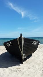 Black boat moored on shore at beach against sky