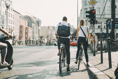 Full length of business coworkers standing with bicycles at road signal in city