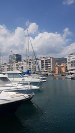 Sailboats moored in sea by buildings against sky