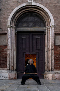 Middle aged tai chi master showing stick exercises outdoors amidst of a medieval cathedral