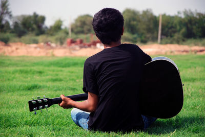 Rear view of man playing guitar while sitting on grass