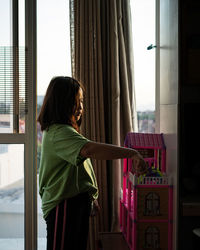 Side view of woman standing by window at home