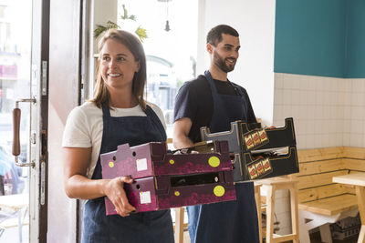 Smiling multi-ethnic salesman and saleswoman carrying crates in restaurant