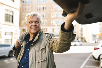 Smiling senior businessman closing car trunk while standing in parking lot