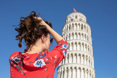 Woman with hand in hair standing against leaning tower of pisa in italy