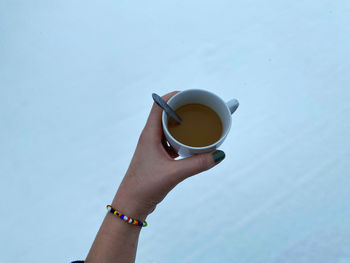 Low angle view of hand holding coffee cup against clear sky