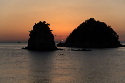 Rock on sea against sky during sunset