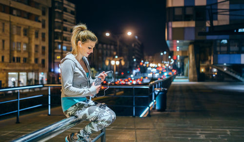 Side view of young woman sitting in city at night