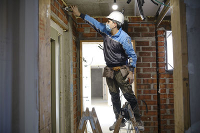 Electrician working with tool standing on ladder at construction site