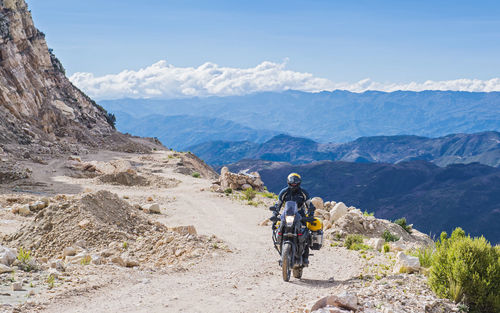 Rear view of man riding motorcycle on mountain against sky
