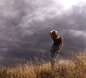 Low angle view of woman standing on field against cloudy sky